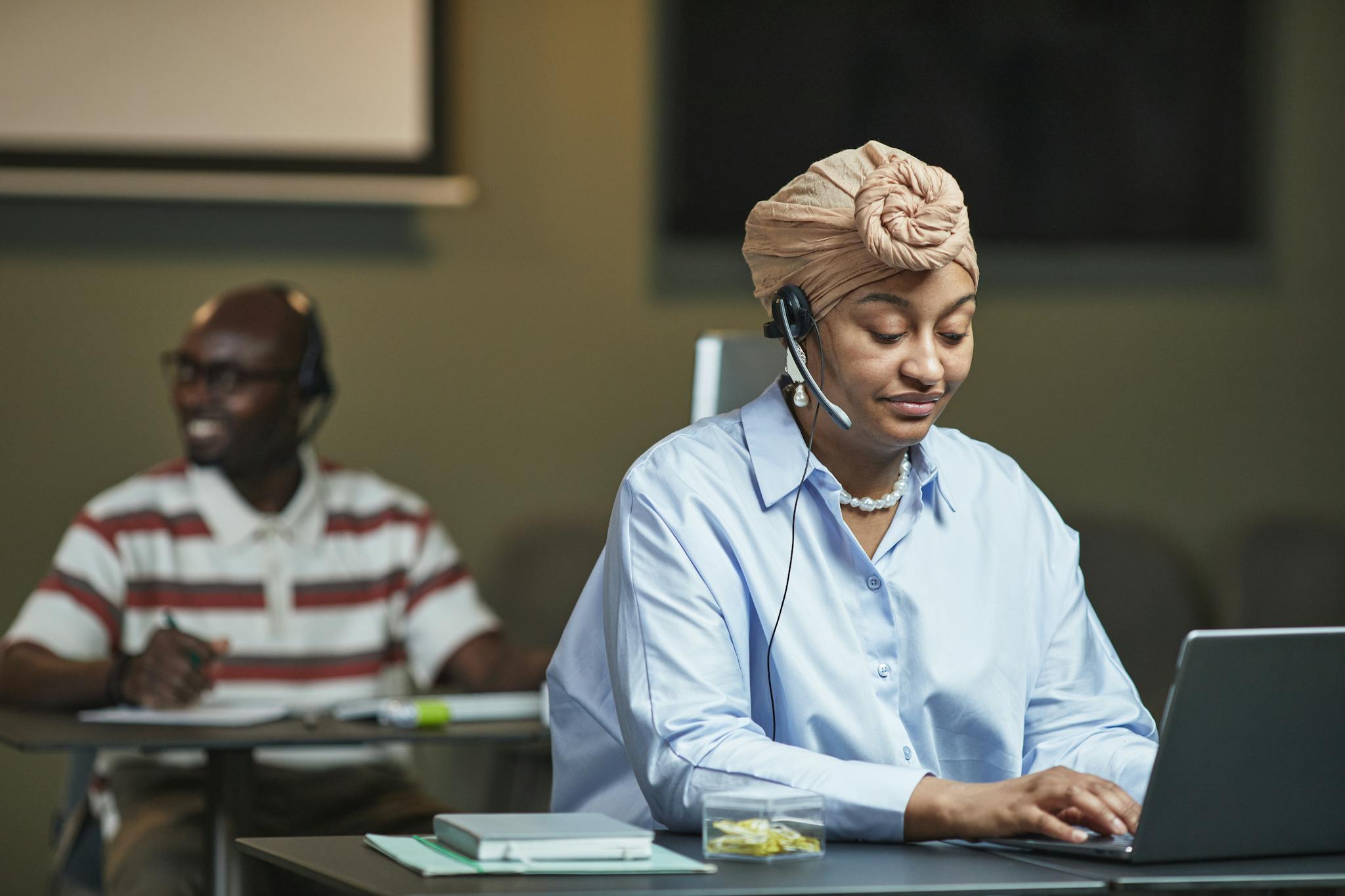 Two call center professionals using headsets and laptops in a modern office environment.